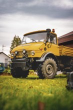 A yellow Unimog stands on a lawn under cloudy sky, tree work, Gechingen, Calw district, Germany