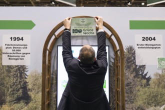 A stand operator hangs up a sign Congratulations to Messe Berlin on 100 years of Green Week at the