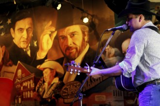 Musician playing guitar in front of detailed wall art with nostalgic flair, Nashville, Tennessee,
