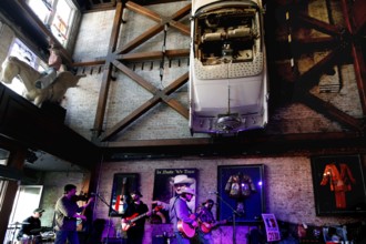 A band plays on a stage surrounded by retro industrial decoration with a car on the wall,