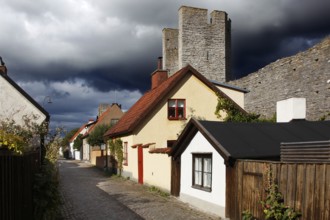 Alley with traditional half-timbered houses and towers of the city wall in Visby under threatening