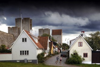 Alley in Visby's old town with historic buildings and city wall towers under a dramatic sky, Visby,