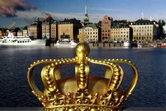 A golden crown in the foreground with a view of the skyline and boats of Stockholm, Stockholm,
