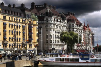 Historic buildings along Strandvägen with boats in water and dramatic sky, Stockholm, Östermalm,
