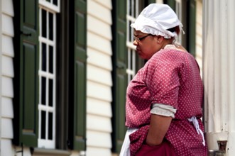 Woman in period clothing looking at a building in Colonial Williamsburg, an impression from