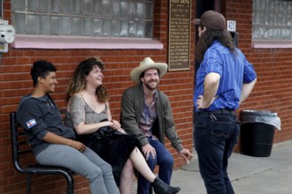 Four people sit relaxed in front of Fred's Lounge and laugh together, Mamou, Louisiana, USA