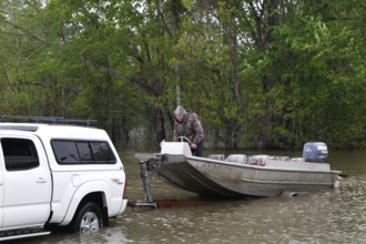 A pickup truck pulls a boat into the water at the Atchafalaya Basin, surrounded by dense forest,
