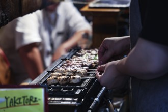 Grilling yakitori skewers in a busy bar setting, Shinjuku, Tokyo, Japan