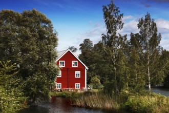 Red house on the riverbank surrounded by lush nature and clear skies, Borensberg, Sweden