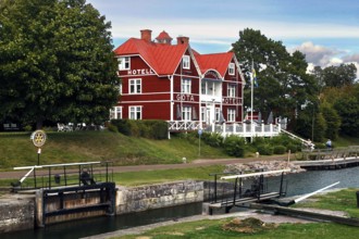 Red Göta Hotel in Borensberg on the Göta Canal next to a lock, surrounded by green trees,