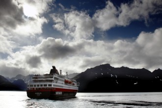 Hurtigruten ship leaves Øksfjord under atmospheric sky, Øksfjord, Norway