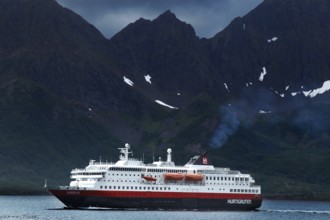 Hurtigruten ship against dramatic mountain backdrop and cloudy sky, Øksfjord, Norway