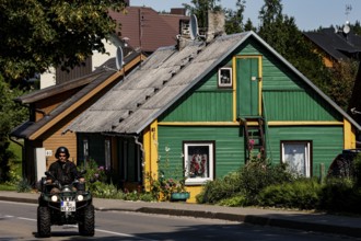 Green wooden house in Trakai with a passing ATV on the road in front of it, Trakai, Lithuania