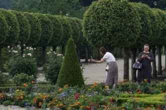 Visitors photograph colorful flowers between perfectly trimmed hedges, Rundale, Latvia