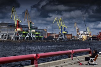 Harbour with cranes and an angler in the foreground under cloudy sky, Ventspils, Latvia