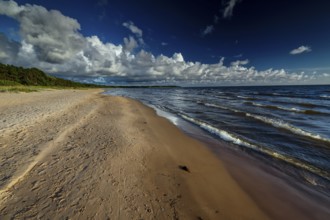Vastness of Vitrupe beach with thick clouds and rolling waves under clear skies, Vitrupe, Latvia