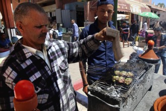 Man grilling traditional Moroccan meat in a busy restaurant, El Kelâa m'Gouna, Morocco