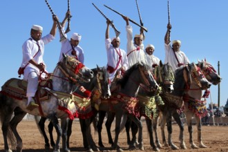 Riders joyfully hold rifles in the air as they sit on magnificently decorated horses in traditional