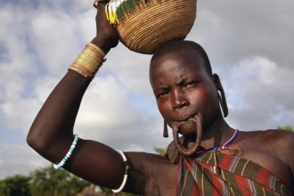 Morsi woman carries a basket on her head and has a lip plate in Mago National Park, Mago National
