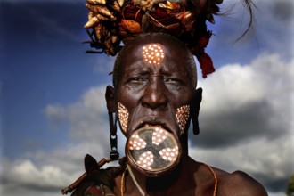 Mursi woman with lip plate and traditional headdress under dramatic sky, Mago National Park,