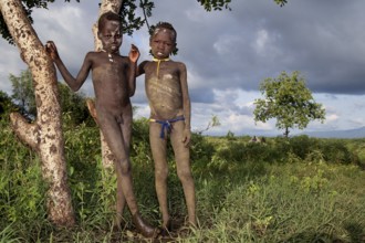 Two Morsi boys stand next to a tree in Mago National Park in Ethiopia, Mago National Park, Ethiopia