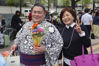 A Sumotori poses with a smiling fan and a bouquet of flowers, Tokyo, Ryogoku, Japan