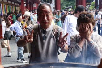 Visitors to Senso-ji Temple pose in front of a large fire bowl, Tokyo, Japan