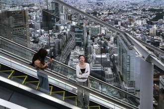 Women ride the escalator in Shibuya with sweeping views over Tokyo, Tokyo, Japan