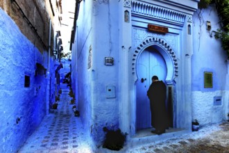 Blue alley with traditional Moroccan gate and a person in the medina of Chefchaouen, Chefchaouen,