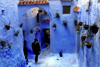 Blue alley with arches and flower pots interspersed with a passing person in the Medina,