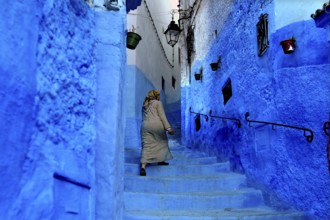 Woman in traditional dress climbing the blue steps of a Medina alley in Chefchaouen, Chefchaouen,