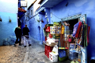 Market stand on a blue wall in the medina of Chefchaouen, people strolling, Chefchaouen, Morocco