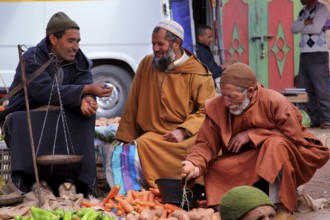 Men wearing traditional clothes at a market in Achaouikh, engaged in conversation, zero
