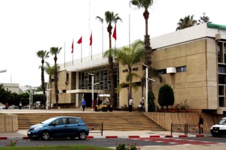Modern building in Agadir with palm tree decoration, flags and a passing car, Agadir, Morocco