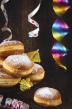 A pile of donuts with powdered sugar, colorful garlands and streamers against a dark wooden