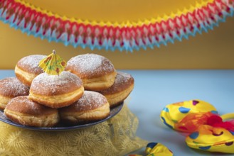 A plate of donuts with powdered sugar on a table surrounded by colorful carnival decoration