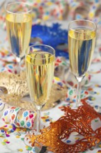 Three champagne glasses with decorative masks with confetti and streamers, carnival