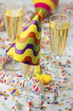 Champagne glasses with colorful party hat surrounded by confetti and streamers, carnival