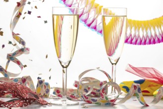 Two filled champagne glasses with colorful streamers, mask and confetti, carnival
