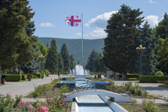 Parkland with central fountain surrounded by flowers and tall trees, Georgian flag, Stalin Park,
