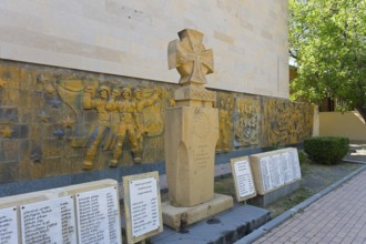 Monument with artistic relief surrounded by memorial plaques in shady surroundings, monument in