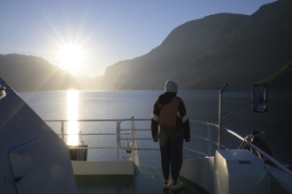 Person standing alone on a ferry at sunset with view of fjord and mountains, view from Columbus
