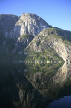 Majestic rocks reflected in clear water under a bright blue sky at Lysefjord, Rogaland, Norway