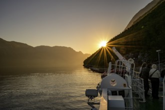 A boat sails through the Lysefjord at sunset with sun star with calm water and surrounded by