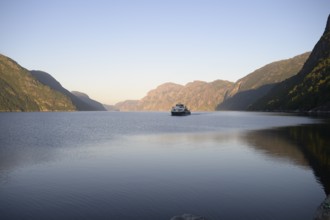 Columbus shipping company ferry in the middle of the quiet Lysefjord at dusk surrounded by