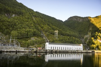 A power plant stands on the banks of a calm body of water de, Lysefjord, nestled in green wooded