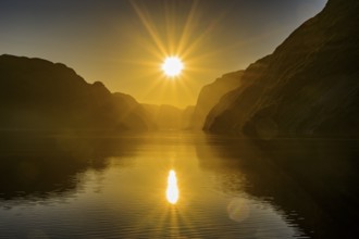 Atmospheric star-shaped sunlight is reflected on quiet fjord waters of Laysefjord between massive