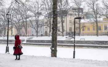 Woman in red winter coat walks along the frozen Aurajoki river, wintery Turku or Swedish Åbo,