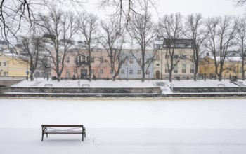 Bench, historic buildings on the frozen Aurajoki River, wintery Turku or Swedish Åbo,