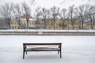 Bench and historic buildings on the frozen Aurajoki river, wintery Turku or Swedish Åbo,